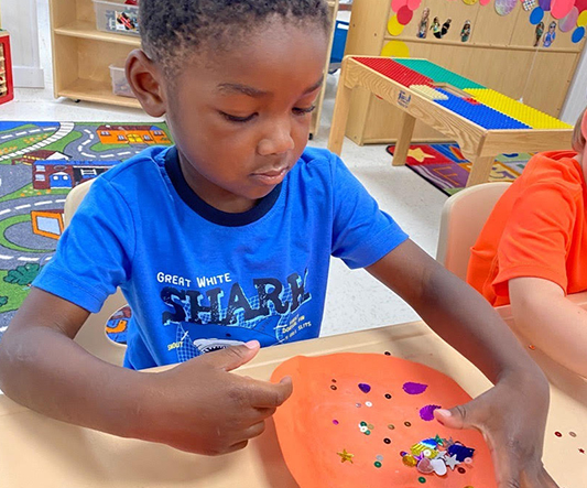 Creating art with sequins and stickers at Playful Minds Learning Center.