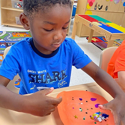Young child making art with cut paper and stickers at our Gerena learning center location.
