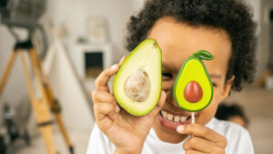 child holding up a toy avocado next to a real one